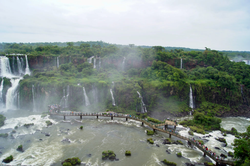 Tiers of cascading waterfalls and a footbridge into the falls. Picture of Iguazu Falls captured from the Brazilian side.