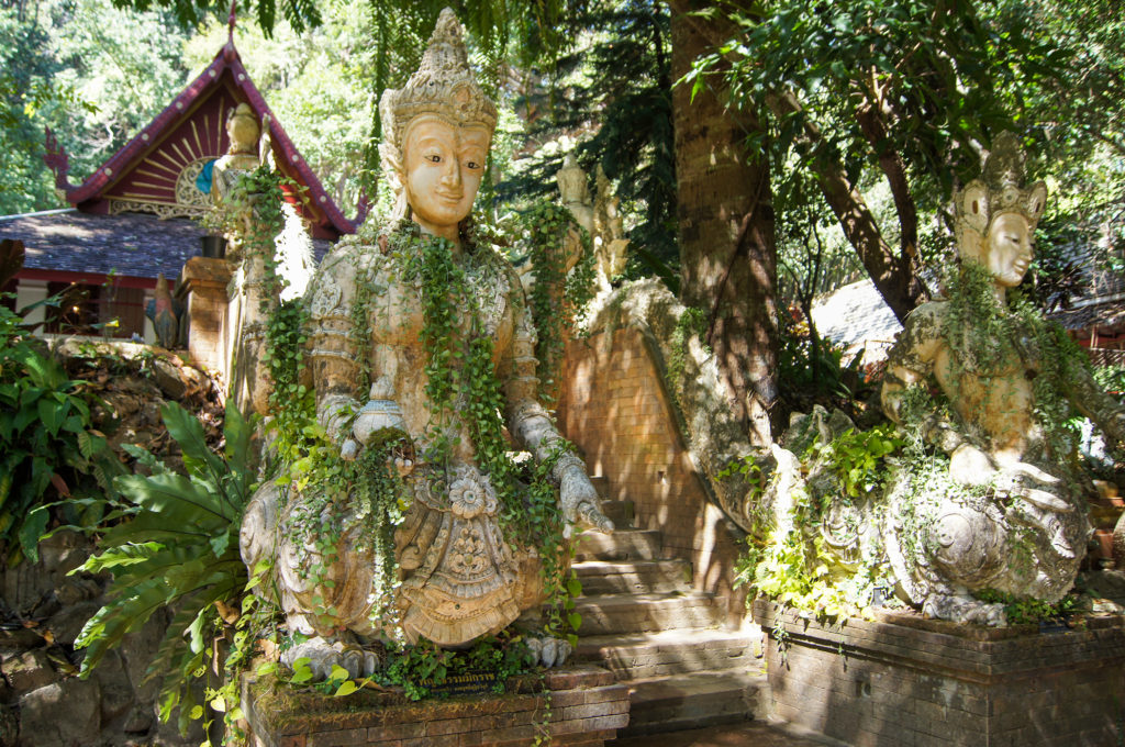 Twin Buddha statues, adorned with jungle vine necklaces, guard the entrance to Wat Pha Lat 
